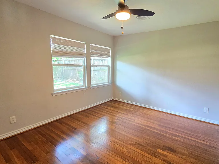 Big primary bedroom with hardwood floors, contemporary ceiling fan, large windows offering natural light.
