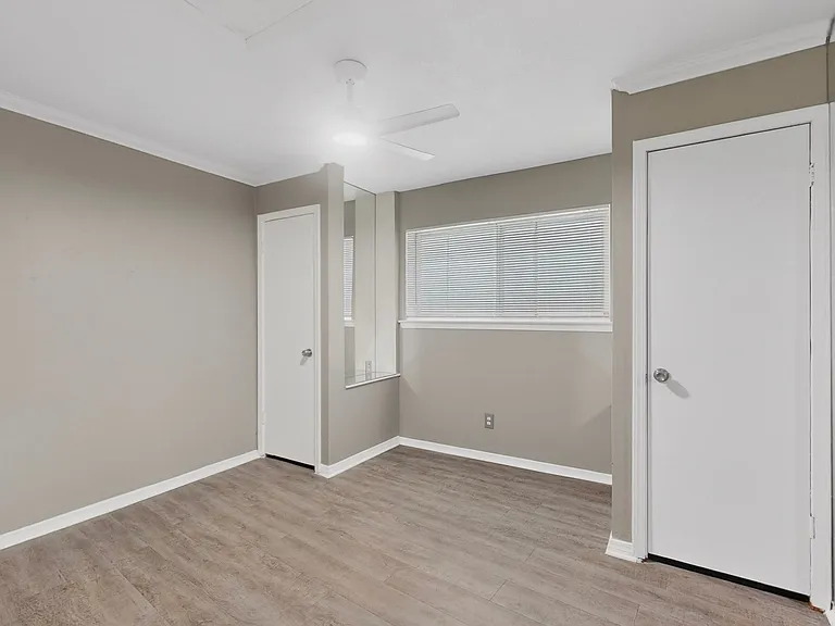 A bright bedroom with a ceiling fan, a wide window and two built-in closets, enhancing the overall comfort of the space.
