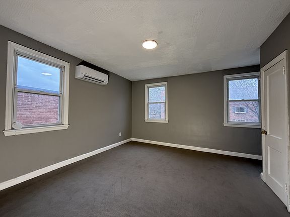 Spacious and bright with plush carpet, large windows, and a sleek wall-mounted AC unit.