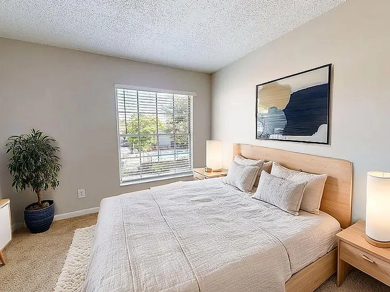 Bright and cozy bedroom featuring a large window, stylish decor, and modern furniture, offering a serene and inviting atmosphere.