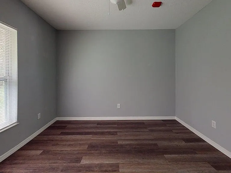 Bright, spacious room with modern gray walls and elegant wooden flooring, complemented by a large window for abundant natural light.