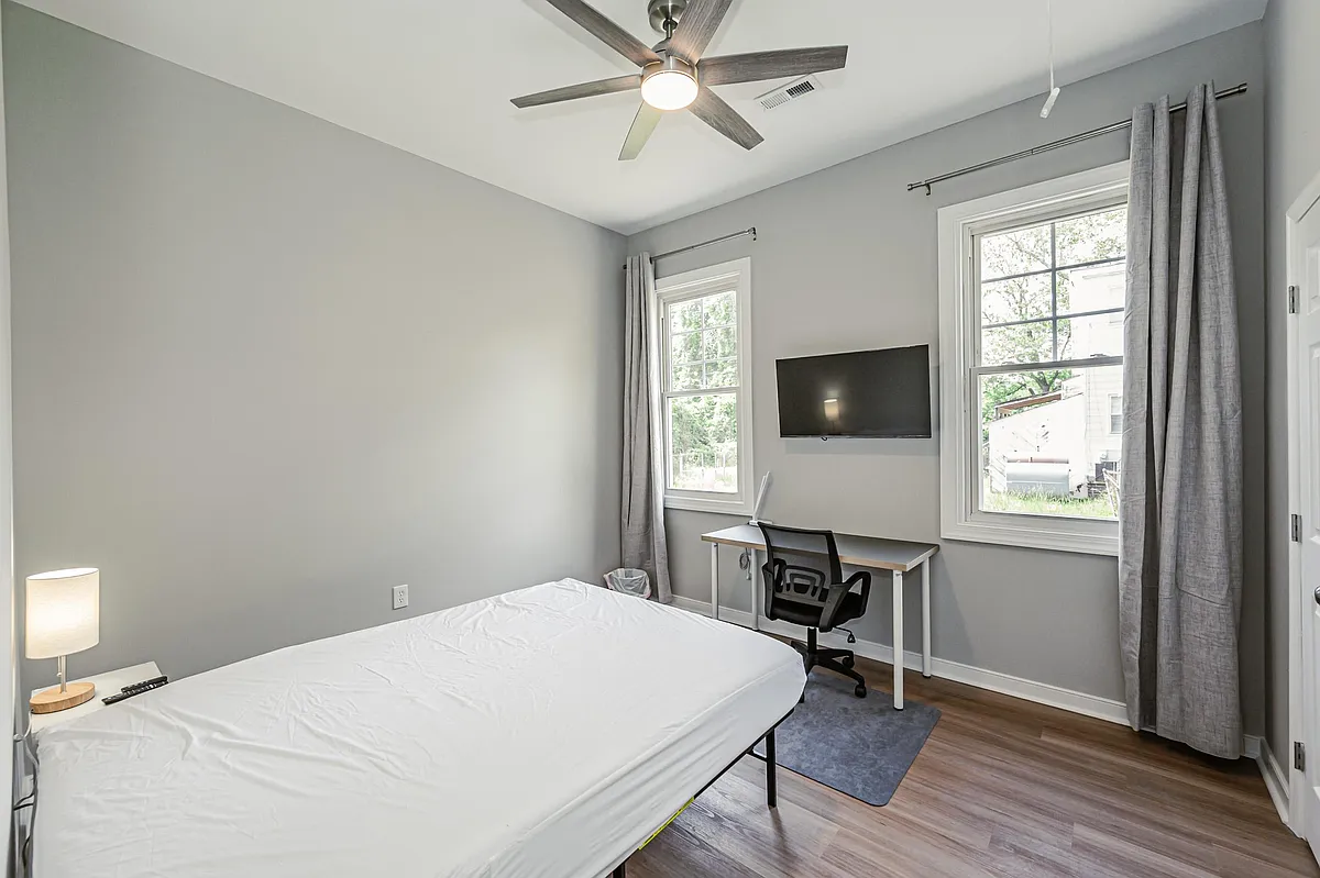 Private bedroom with two windows, ceiling fan, wall-mounted TV, and a dedicated desk area with chair for studying or WFH. - Greenwood Rd