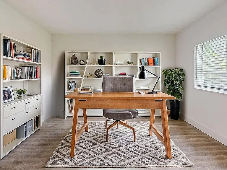 Contemporary home office with a sleek wooden desk, stylish chair, and well-organized bookshelves, illuminated by natural light from a large window.