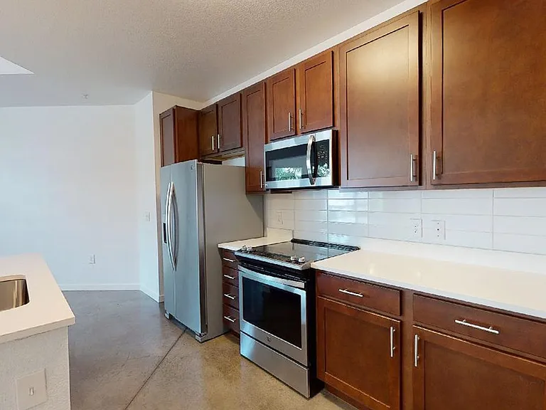 Apartment kitchen with stainless steel appliances, quartz countertops and polished concrete flooring.