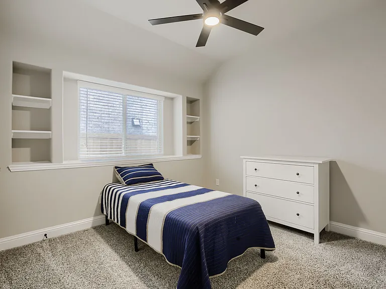 Carpeted room featuring a ceiling fan with integrated lighting, built-in shelving, and a window with blinds