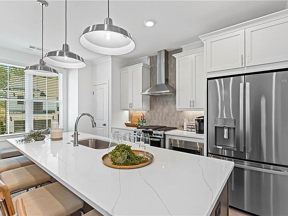 Kitchen featuring stainless steel appliances, wall chimney exhaust hood, a center island with sink,
