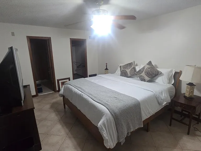 Spacious bedroom with a full bed, nightstand lighting, and tile flooring, plus direct access to an adjacent room/closet area.