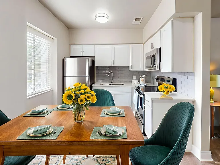 Charming kitchen and dining area with sleek white cabinets, elegant wooden table set with modern dishware, vibrant sunflowers, and cozy seating, perfect for hosting intimate gatherings.