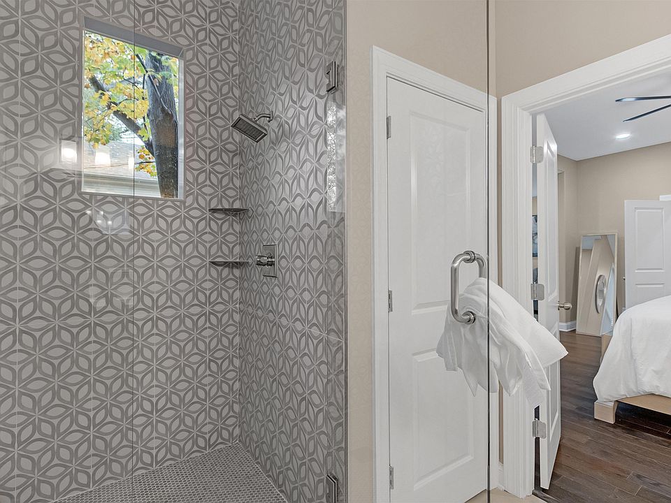 Walk-in glass shower with patterned tile surround, built-in shelving, and a window for natural light.