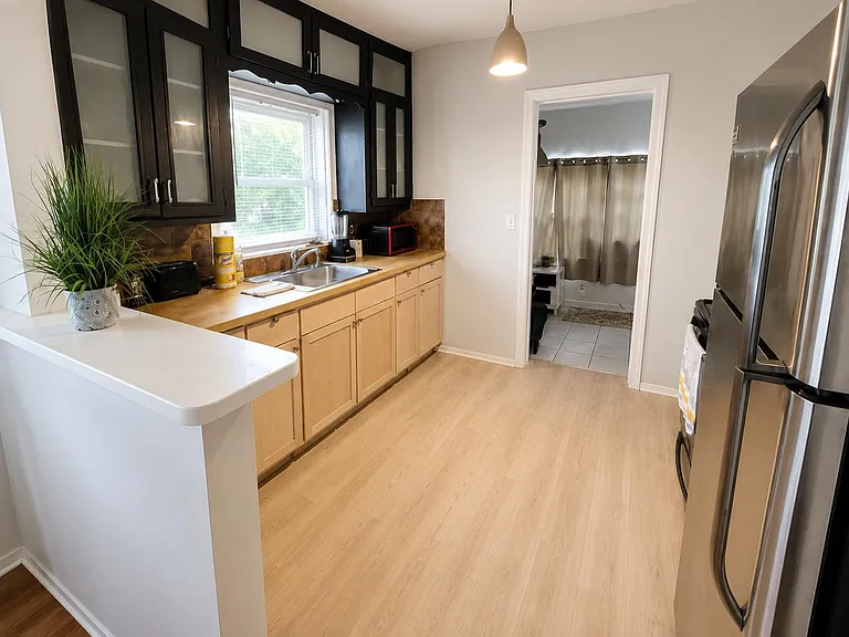 Galley kitchen with stainless-steel fridge, ample cabinetry, long counters, and a sink set beneath a window.