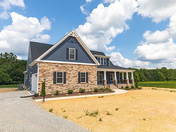 Two-story house with stone and blue siding, large porch, and gravel driveway under a partly cloudy s