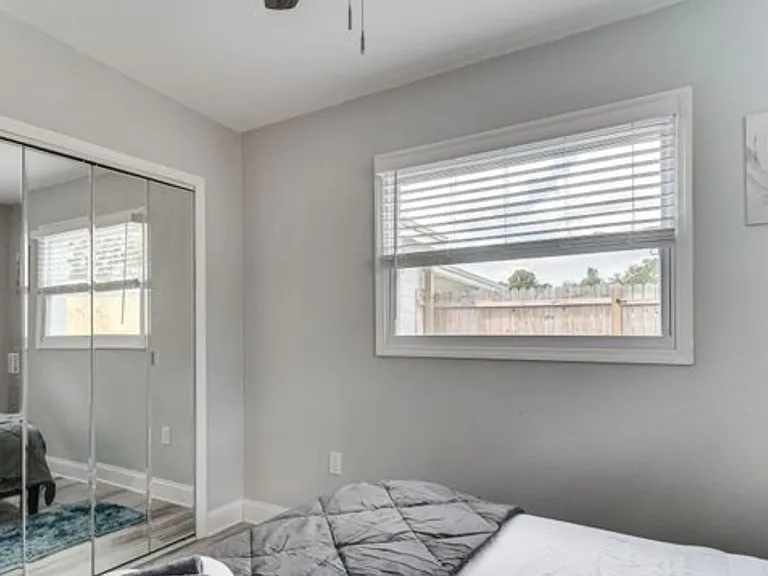 Bedroom with mirrored sliding closet doors, a window with blinds, and neutral finishes for flexible furnishing.