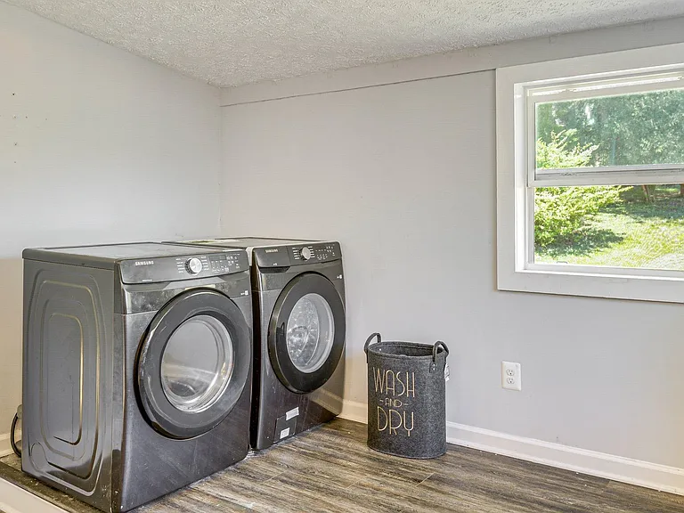 Dedicated laundry area with full-size front-load washer and dryer, durable flooring, and a window with yard views.
