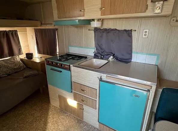 Compact kitchenette with cooktop, sink, under-counter fridge, and upper/lower cabinetry for convenient meal prep.