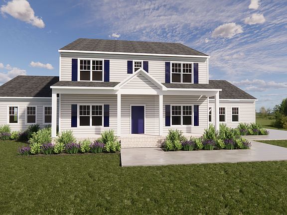 A two-story gray house with a gable roof in Belleair, surrounded by a green lawn and shrubs, under a