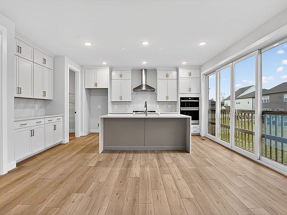 A modern, bright kitchen with white cabinets, a gray island, and large windows overlooking a backyar