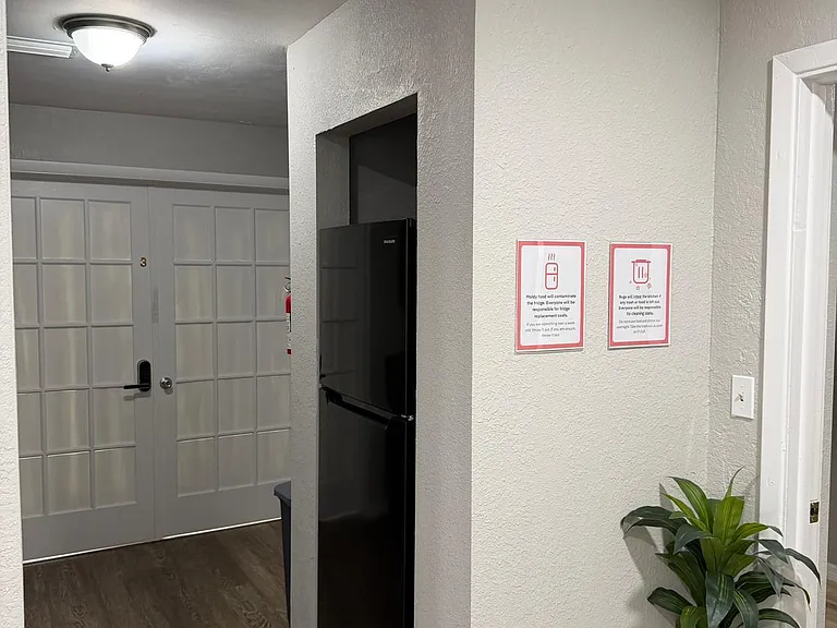 Hallway area with wood-look flooring, neutral walls, ceiling lighting, and a recessed nook with a full-size refrigerator.