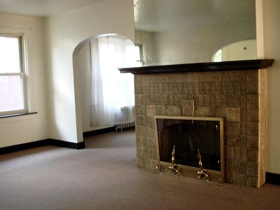 Living room with open arched entry to the dining room. Decorative tile fireplace and wood mantlepiece. The mirror image above the mantle reflects the archway to the sunroom.