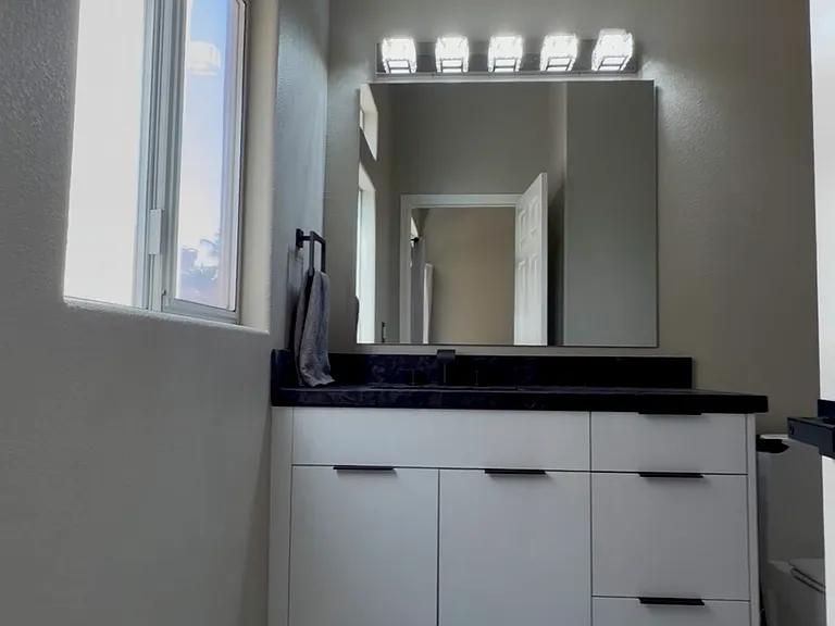 Private office bathroom featuring high-gloss white cabinetry and granite counter