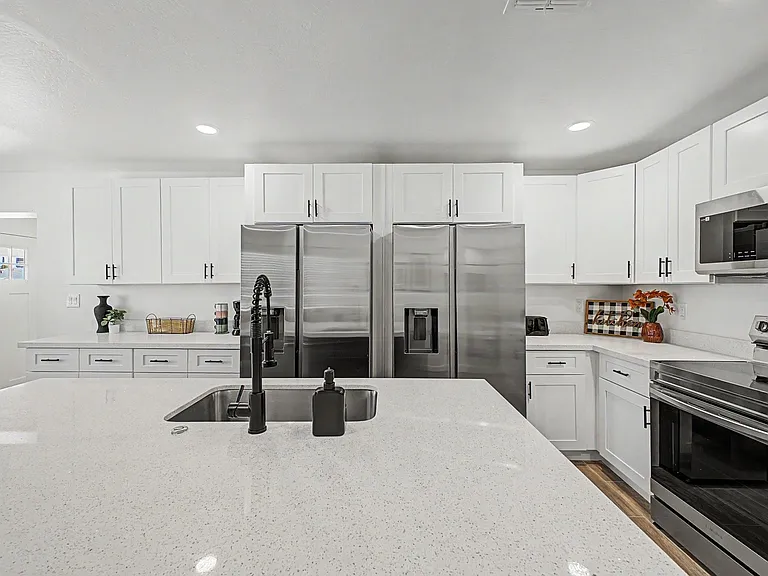 Spacious kitchen with a large island, double sink, stainless appliances, and abundant shaker cabinetry for storage.