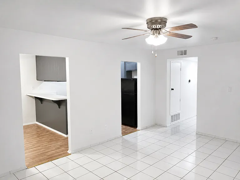 Bright and open living area with tile flooring, ceiling fan, fireplace, and easy access to the kitchen and hallway.