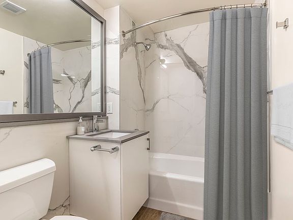 Renovated II North/South bath with grey quartz countertops, white lacquer cabinetry, marble surrounding, and hard surface flooring