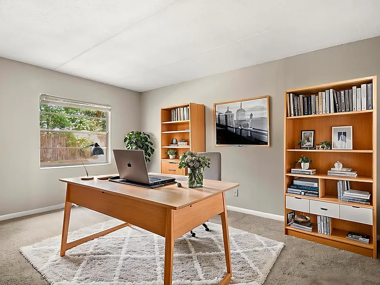 Bright and sophisticated home office with stylish desk, bookshelves filled with books and decor, a large window allowing natural light, and elegant artwork on the wall.