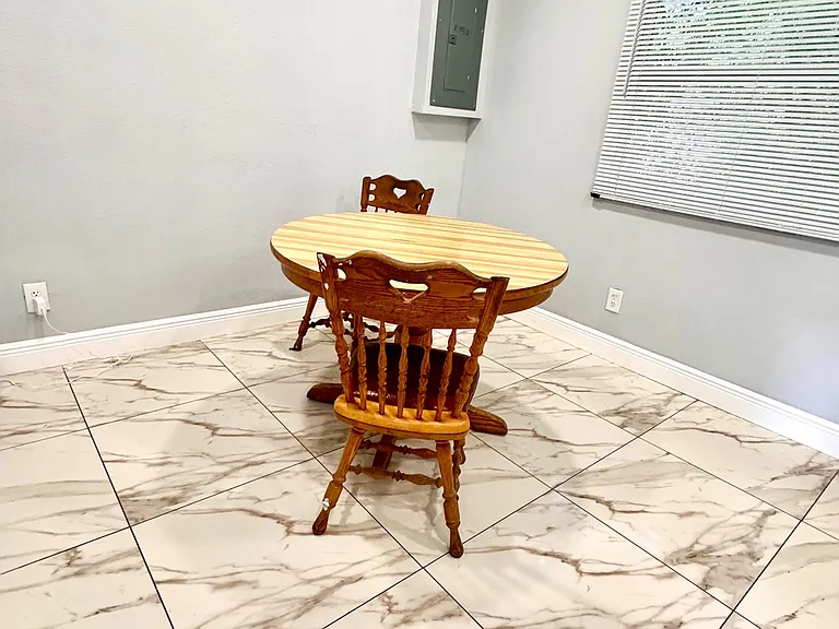 Dedicated dining nook with a round table setup, tiled flooring, and a window with blinds for natural light.