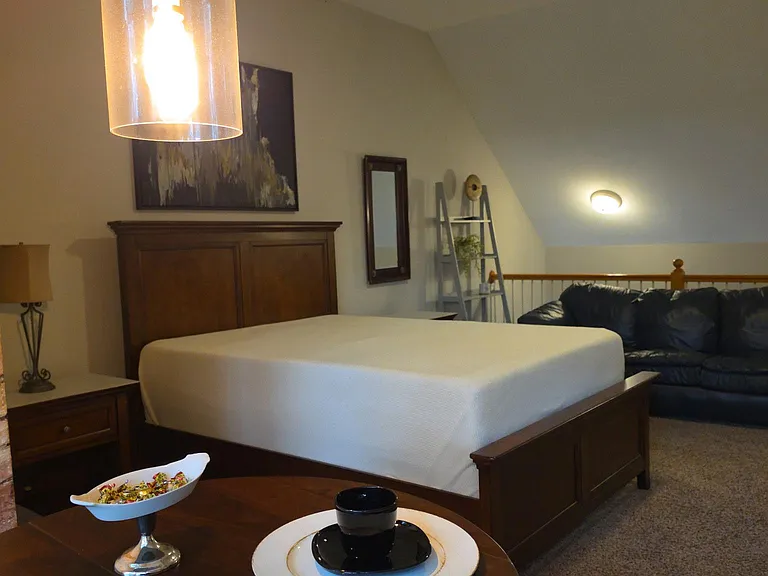 Spacious sleeping area with a full bed, ceiling fan, and convenient nearby seating for relaxing or reading.