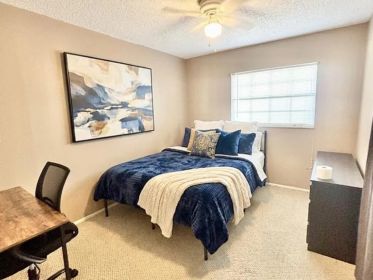 Comfortable bedroom with a full bed, work desk, dresser storage, and a window with blinds plus ceiling fan lighting.