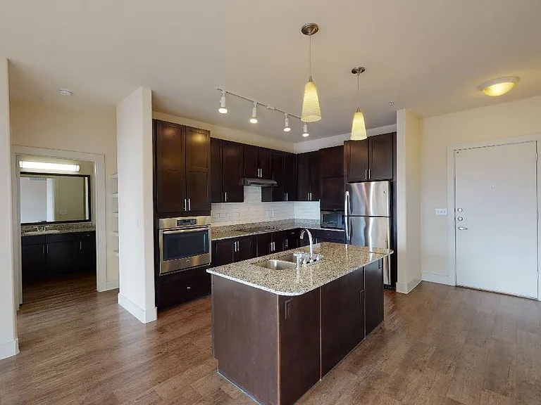 Apartment kitchen with stainless steel appliances in select homes, granite countertops and wood-style flooring.