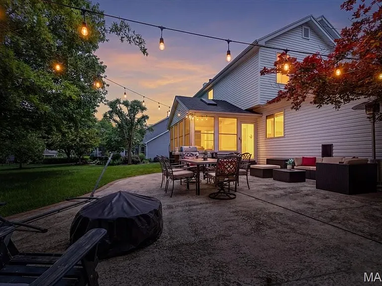 Spacious concrete patio featuring string lighting, an enclosed sunroom, a vibrant red tree, and a large grassy area