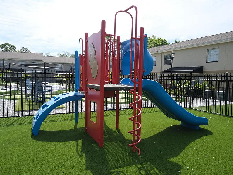 Vibrant playground with colorful slides and climbing structures on lush green turf, perfect for family-friendly living.