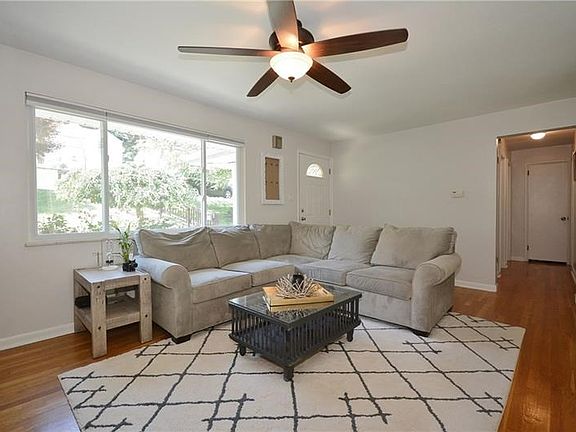The sunlit living room features beautiful hardwood floors and neutral painted walls. The hallway leads to the three bedrooms.
