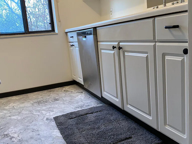 New white & gray marble look vinyl in staggered brick pattern, stainless steel front on dishwasher, off white Roman shade.