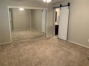 Plush carpeted room featuring a mirrored closet with sliding doors, a ceiling fan, and a white barn door