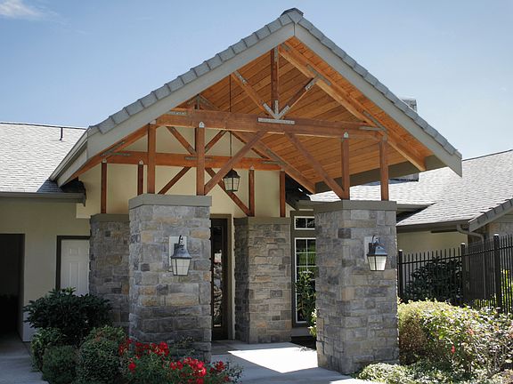 Inviting entrance with charming stone columns, elegant wooden beams, and lush greenery, showcasing modern architectural design.