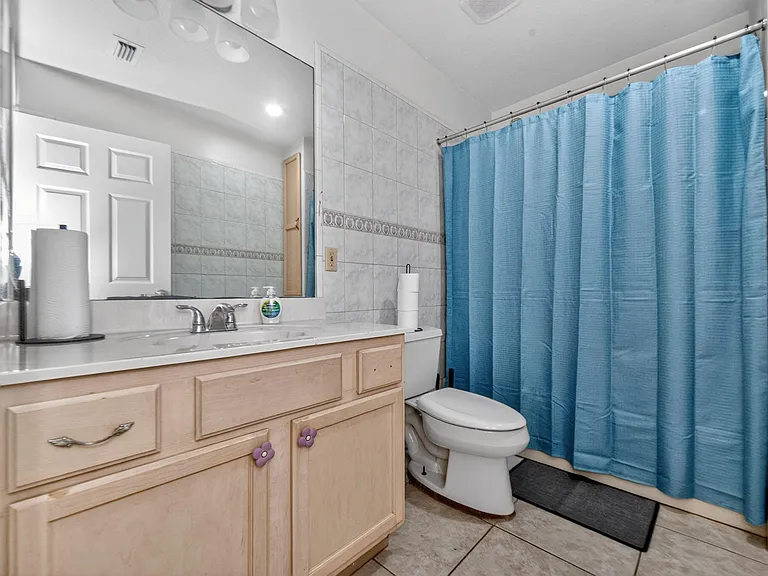 Full bathroom with tiled tub/shower, single-sink vanity with storage, and a large mirror for daily routines.