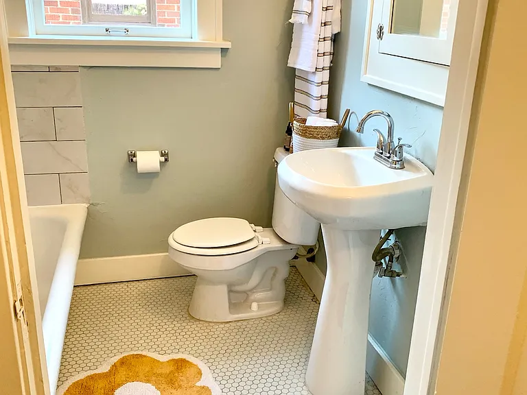 Fully restored and updated bathroom with tub, shower, medicine cabinet, and ample linen storage.