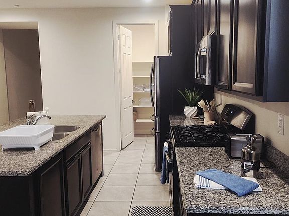 Galley kitchen with granite counters, dark cabinetry, gas range, and stainless refrigerator, plus a pantry for extra storage.