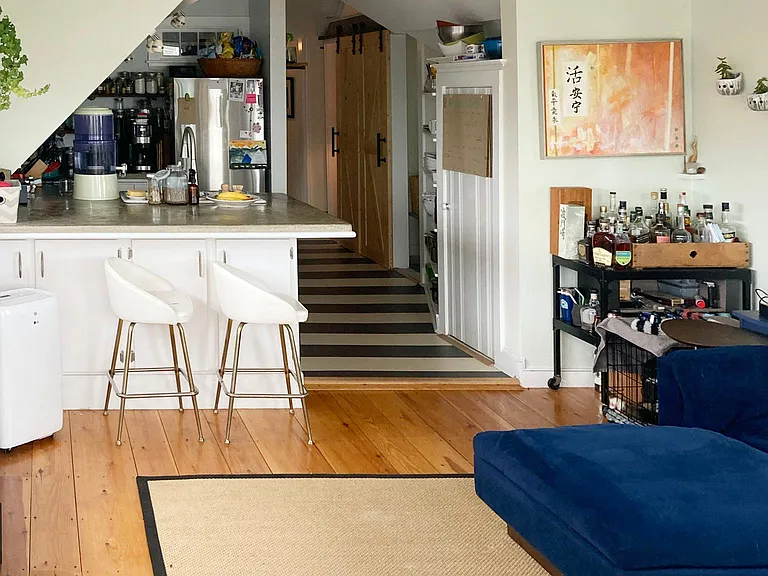 Living area with open kitchen, wide plank floors, and exposed beams.