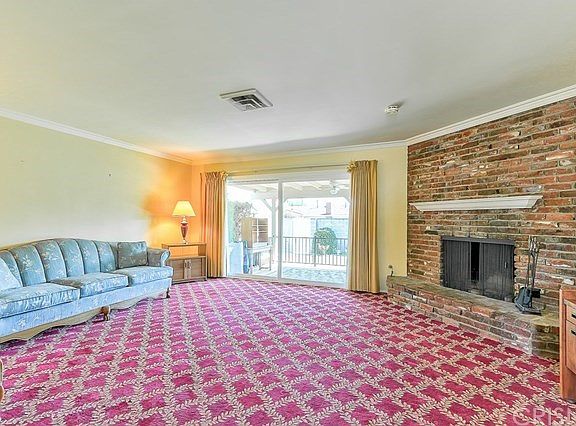 Living room with brick fireplace, crown molding, and large dual paned slider leading out to the giant covered patio.