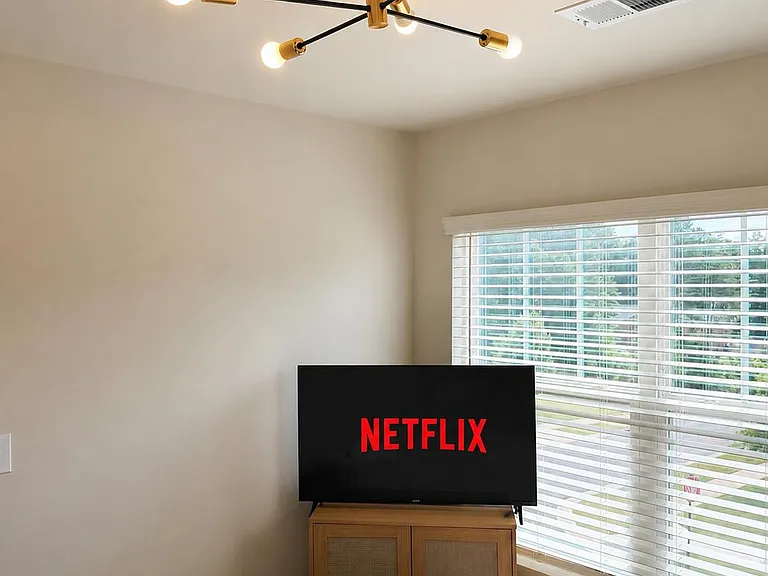 Bedroom with a large window and blinds, plus a TV setup and overhead light for comfortable everyday living.