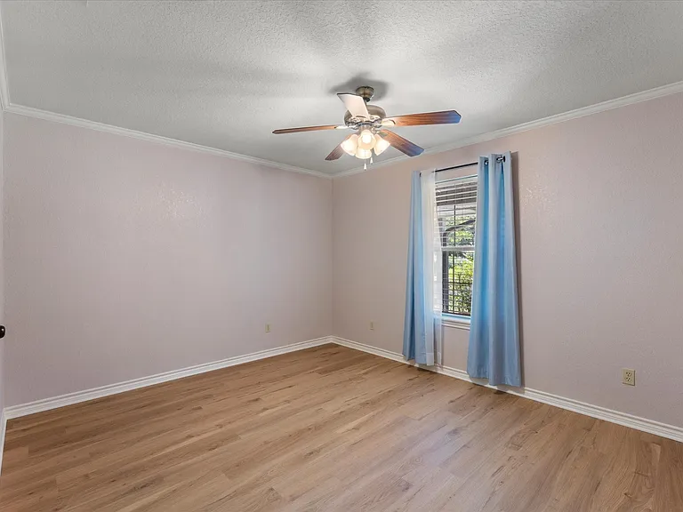 Light-filled room featuring wood-finish flooring, a ceiling fan with integrated lighting, and crown molding