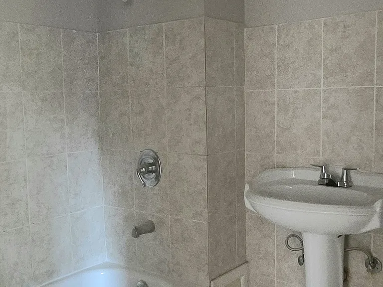 The spacious bathroom has a new toilet, large pedestal sink and classic prewar high ceilings.