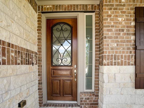 The front door is is a beautiful stained wood with a fabulous iron metal accent. Both of the glass coverings on the door and side window are covered with an opaque covering for privacy.