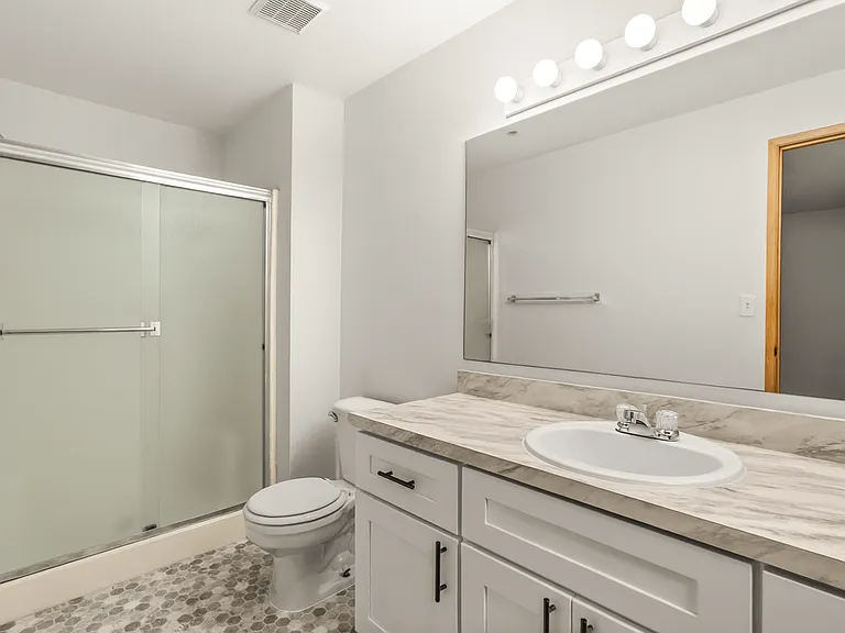 Updated bathroom featuring a spacious vanity, marble-style counters, and a walk-in shower with sliding glass doors. Updated bathroom featuring a spacious vanity, marble-style counters, and a walk-in shower with sliding glass doors.