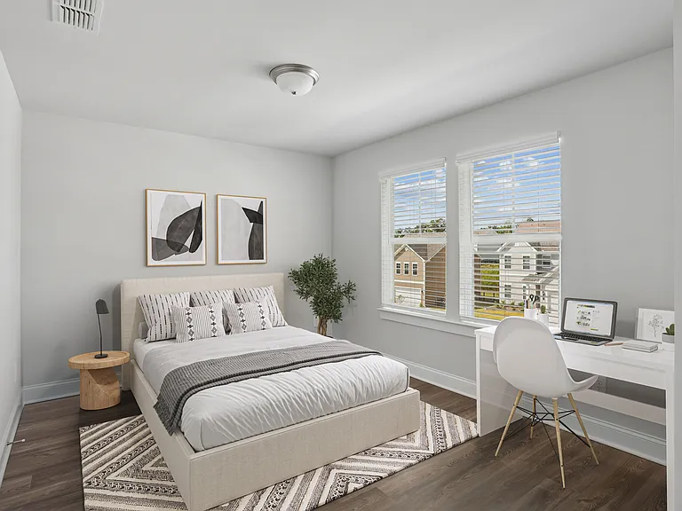 Secondary bedroom with queen bed, large sunlit window, and workspace with desk and chair.