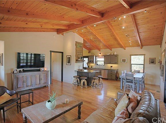 Great room has teak flooring, high exposed-beam ceiling, eating bar and also dining area, all open to the kitchen.