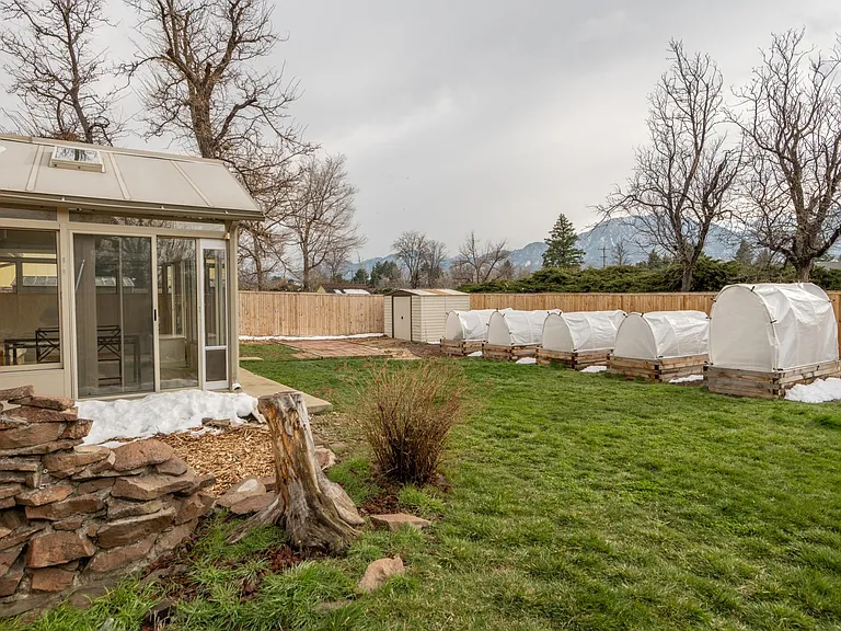 Back yard looking towards Bear Peak. Shown are a decorative wall, the sun room, storage shed, lawn, and the raised garden beds.